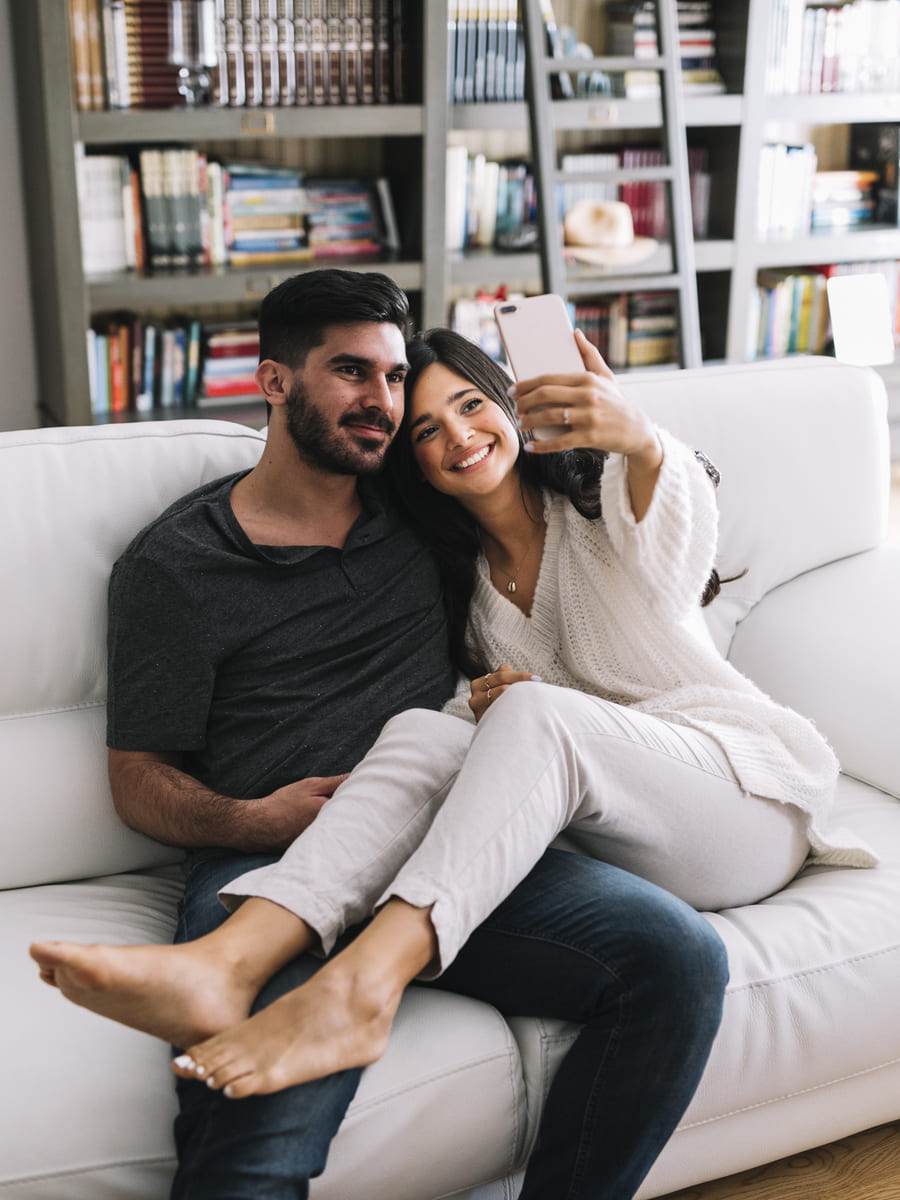 mujer sonriente sentada su novio tomando selfie sofá