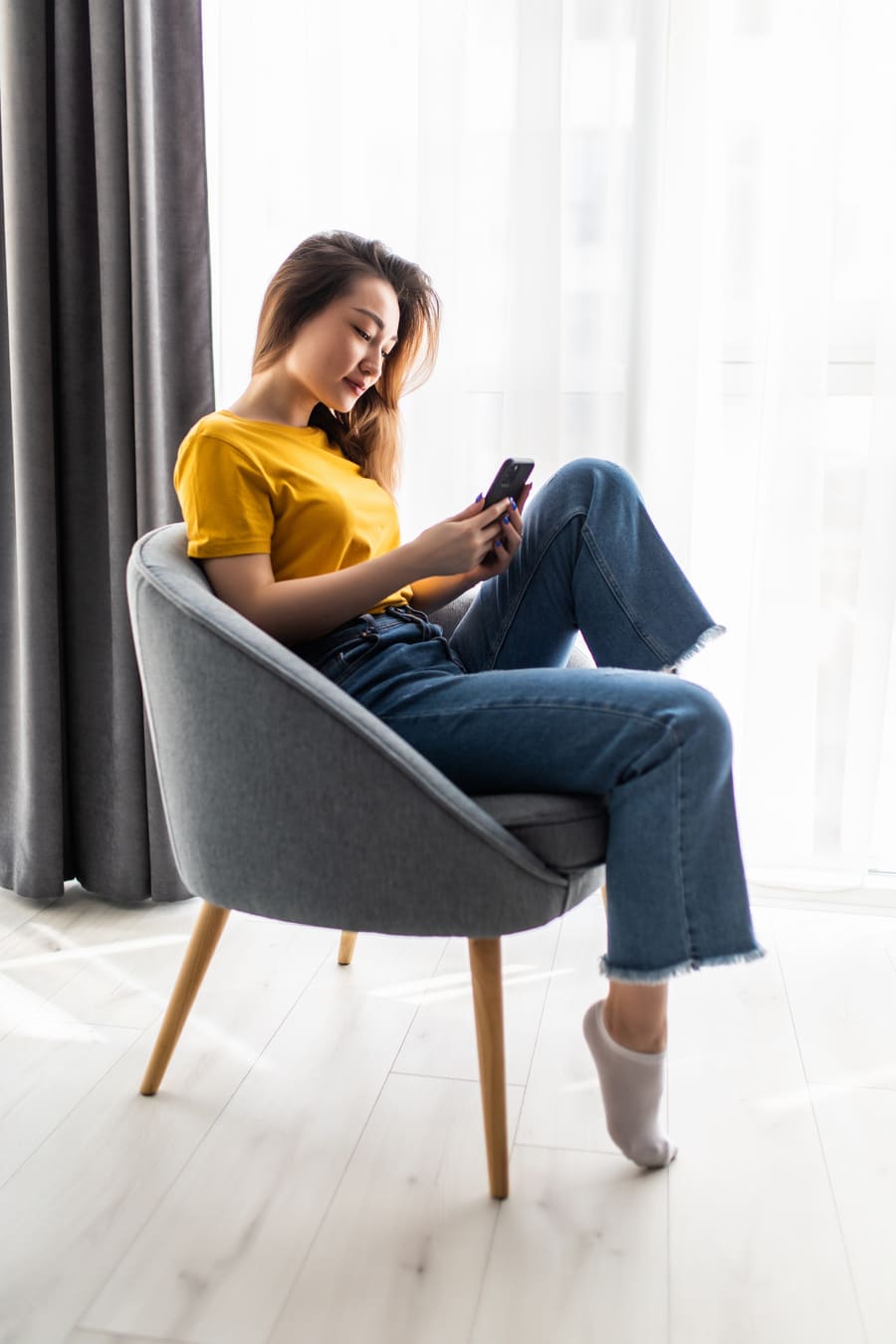 joven mujer asiática usando teléfono móvil sentada silla sala interior