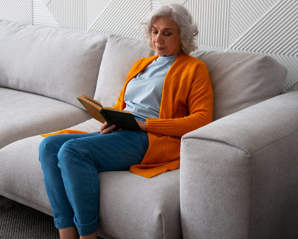 mujer mayor usando tablet sentada en sofa gris en salon con decoracion moderna